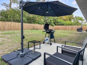 Enjoy al fresco dining on the patio, where a grill and table with chairs await, shaded by a large umbrella.