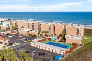 Un hotel de varios pisos con piscina en la azotea, estacionamiento y vista al océano.