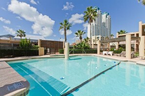 Una piscina con agua azul cristalina, rodeada de palmeras y un edificio moderno al fondo.