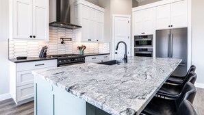 A modern kitchen with white cabinets, a granite island, stainless steel appliances, and a hexagonal backsplash. - Desert Dreaming 2 Bedroom, Den, Pet Friendly, Hot Tub EV Charger (Washington)
