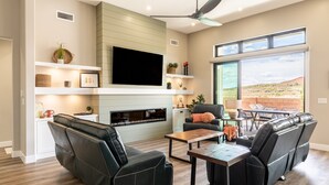A modern living room with a fireplace, black leather sofa, and a dining area with a table and chairs. - Desert Dreaming 2 Bedroom, Den, Pet Friendly, Hot Tub EV Charger (Washington)