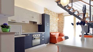 A modern kitchen with grey and black cabinets, a built-in oven, and a dining area with a white table and orange chairs. - Villa with pool near the beach (Banjole)