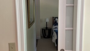 Een gang met een tapijtvloer die leidt naar een slaapkamer met een bed en nachtkastje.