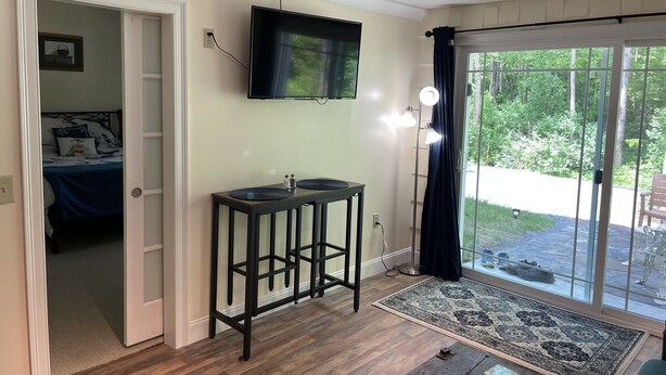 Een kamer met een bed, een aan de muur bevestigde televisie, een tafeltje met een lamp en uitzicht op een tuin door een schuifdeur.