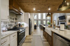A spacious kitchen with a stone wall, wooden ceiling, and a large island with a dishwasher.