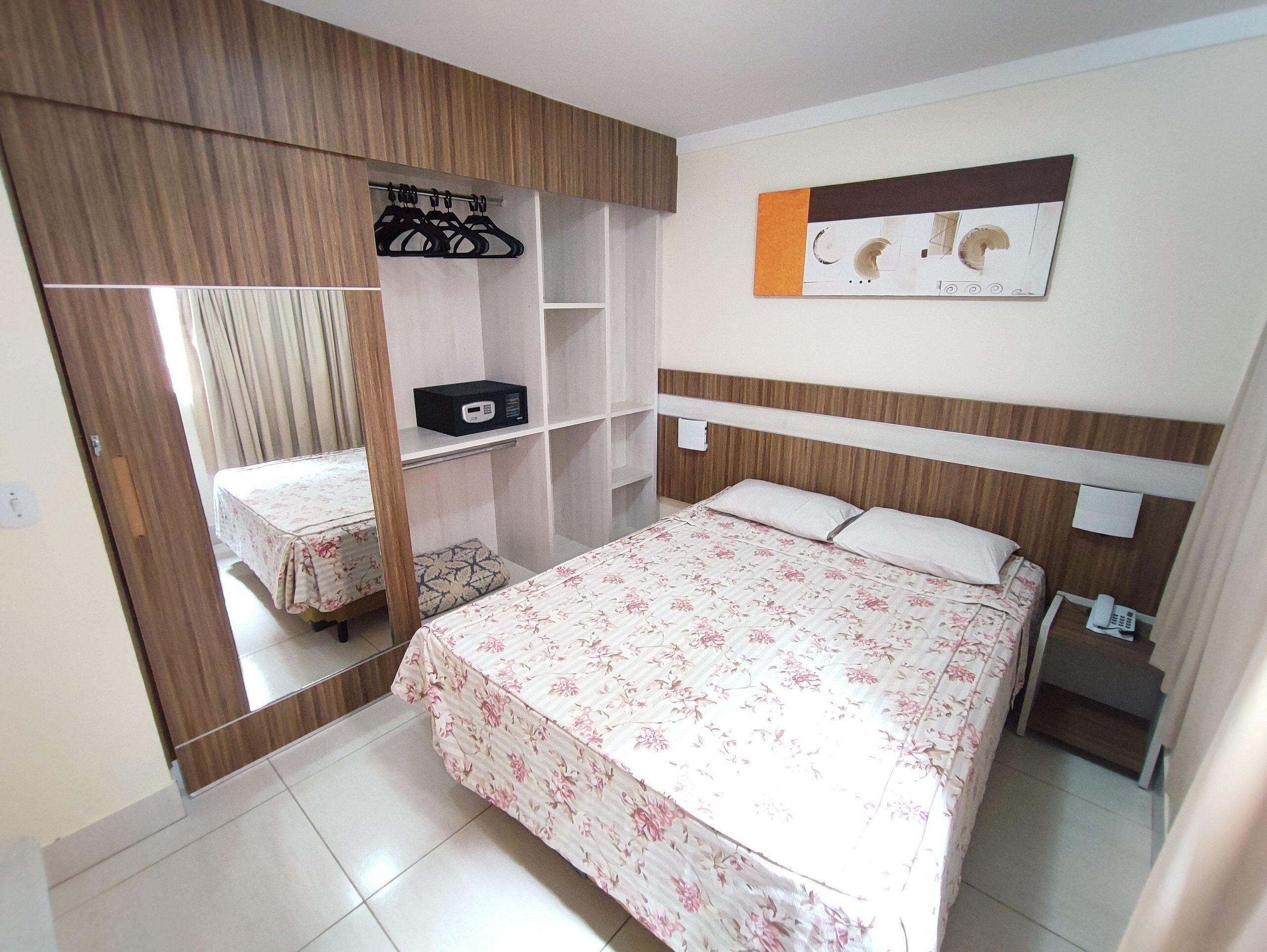 Un dormitorio con cama, armario, mesita de noche y estante en la pared.