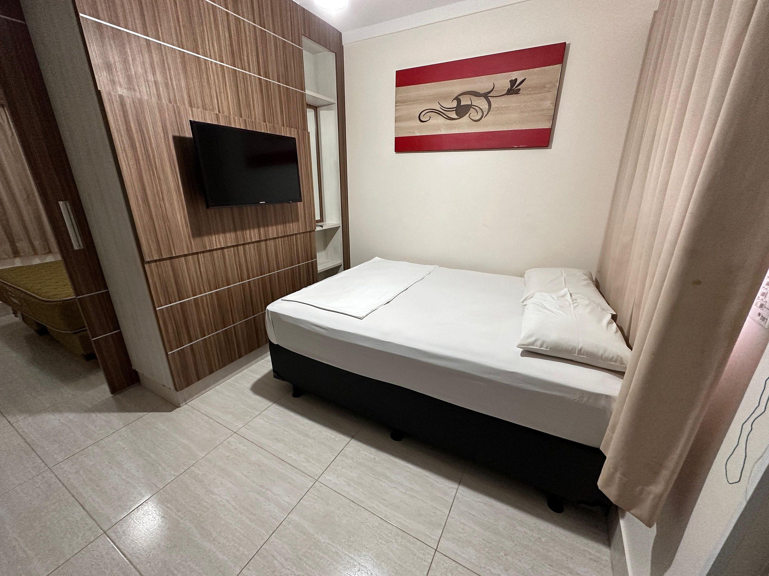 Quarto com cama, televisão fixada na parede e guarda-roupa de madeira.