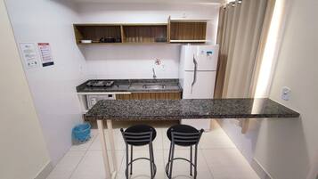 Cozinha compacta com bancada de granito, dois banquetes, geladeira e armários de madeira.