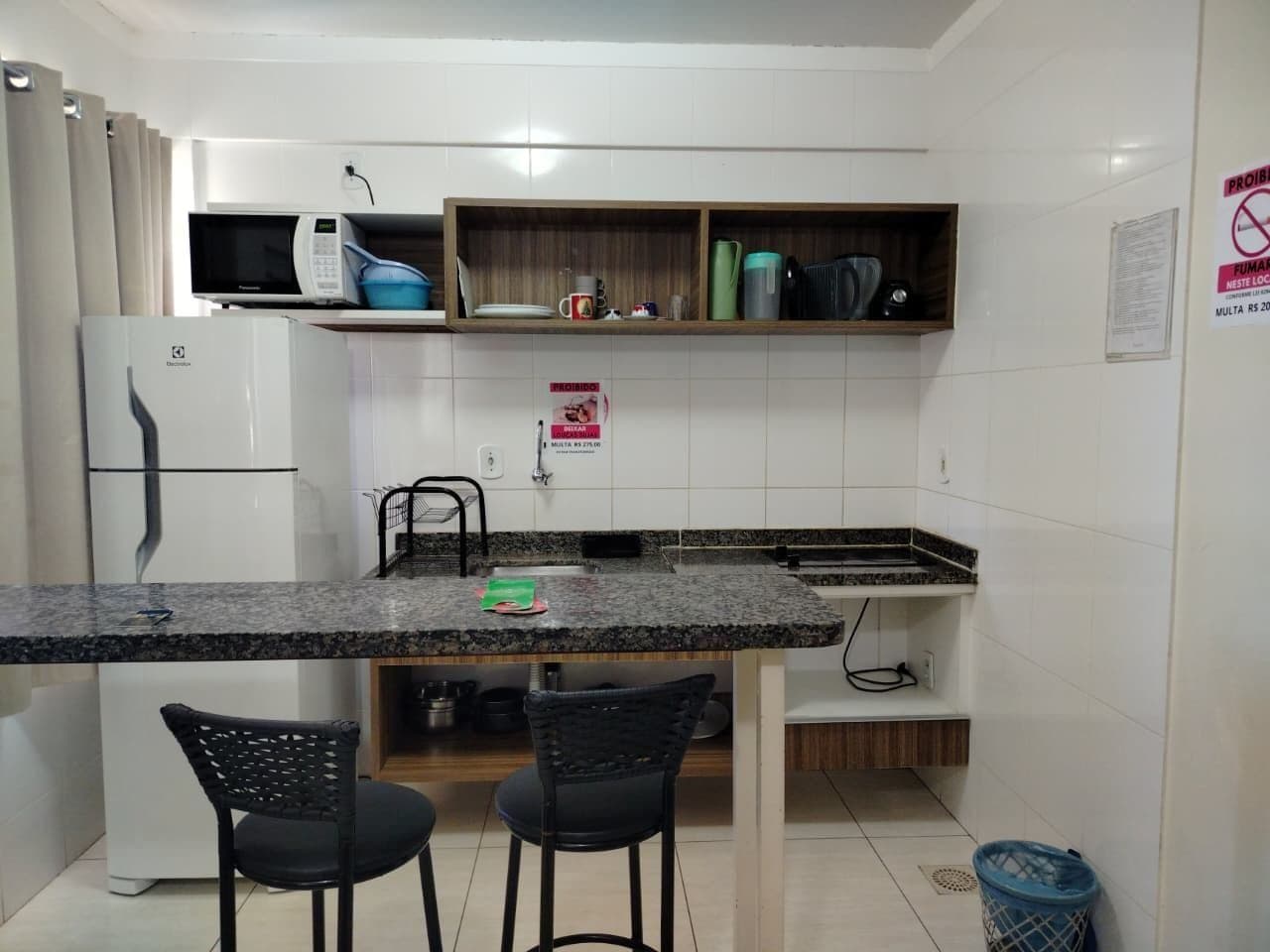 Una cocina compacta con microondas, refrigerador y pileta. Hay dos sillas y un estante pequeño sobre la encimera.