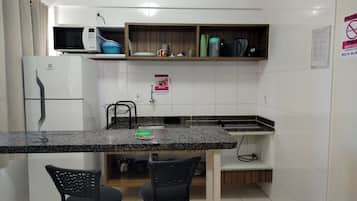 Una cocina compacta con microondas, refrigerador y pileta. Hay dos sillas y un estante pequeño sobre la encimera.