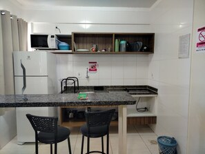 Una cocina compacta con microondas, refrigerador y pileta. Hay dos sillas y un estante pequeño sobre la encimera.