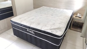 Ein Bett mit einer Matratze der Marke Magestic, ein hölzernes Kopfende, ein Nachttisch mit einem Telefon und eine grüne Wanddekoration.