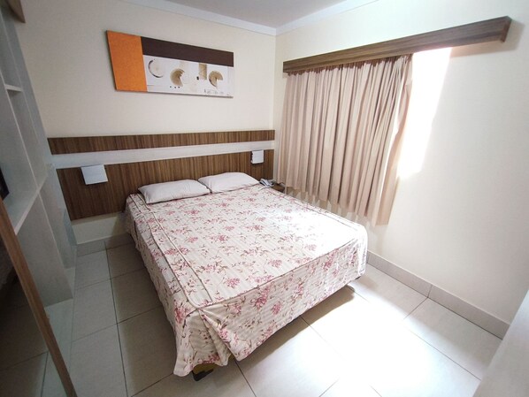 Un dormitorio con cama, cabecera, ventana con cortinas y una obra de arte en la pared.