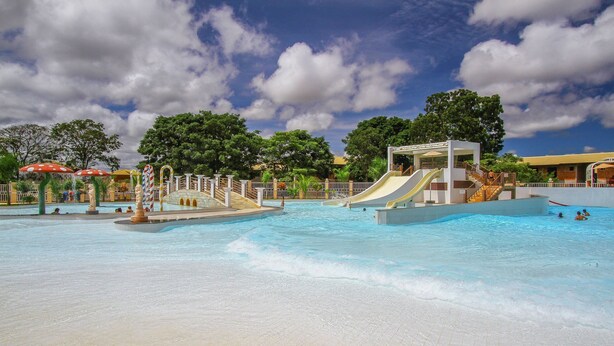 Parque acuático con una piscina grande, toboganes y una zona cubierta con sombrillas.
