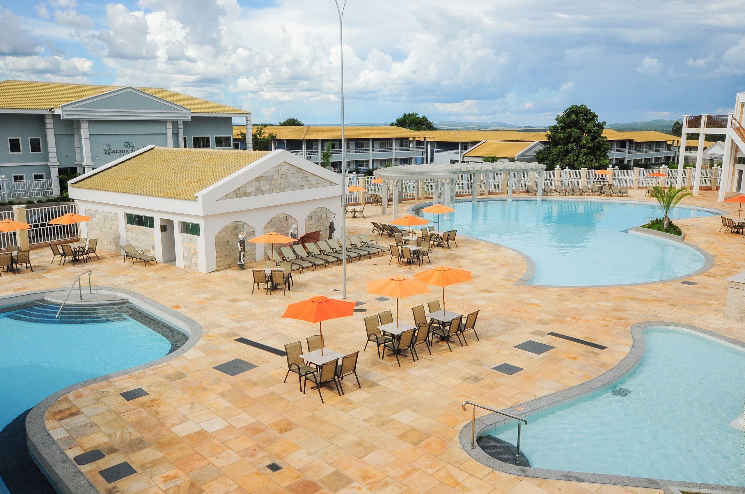 Resort com uma grande piscina, áreas de estar ao ar livre com guarda-sóis e um edifício com telhado amarelo.