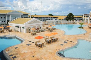A resort with a large swimming pool, outdoor seating areas with umbrellas, and a building with a yellow roof. - LACQUA II (Caldas Novas)