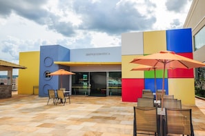 Un patio al aire libre con mesas y sillas, una pared de colores y un letrero que dice 'BRINQUEDOTECA'.