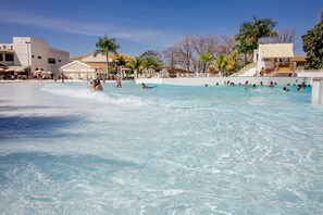 Un área de piscina con agua cristalina, palmeras y un edificio de fachada blanca.