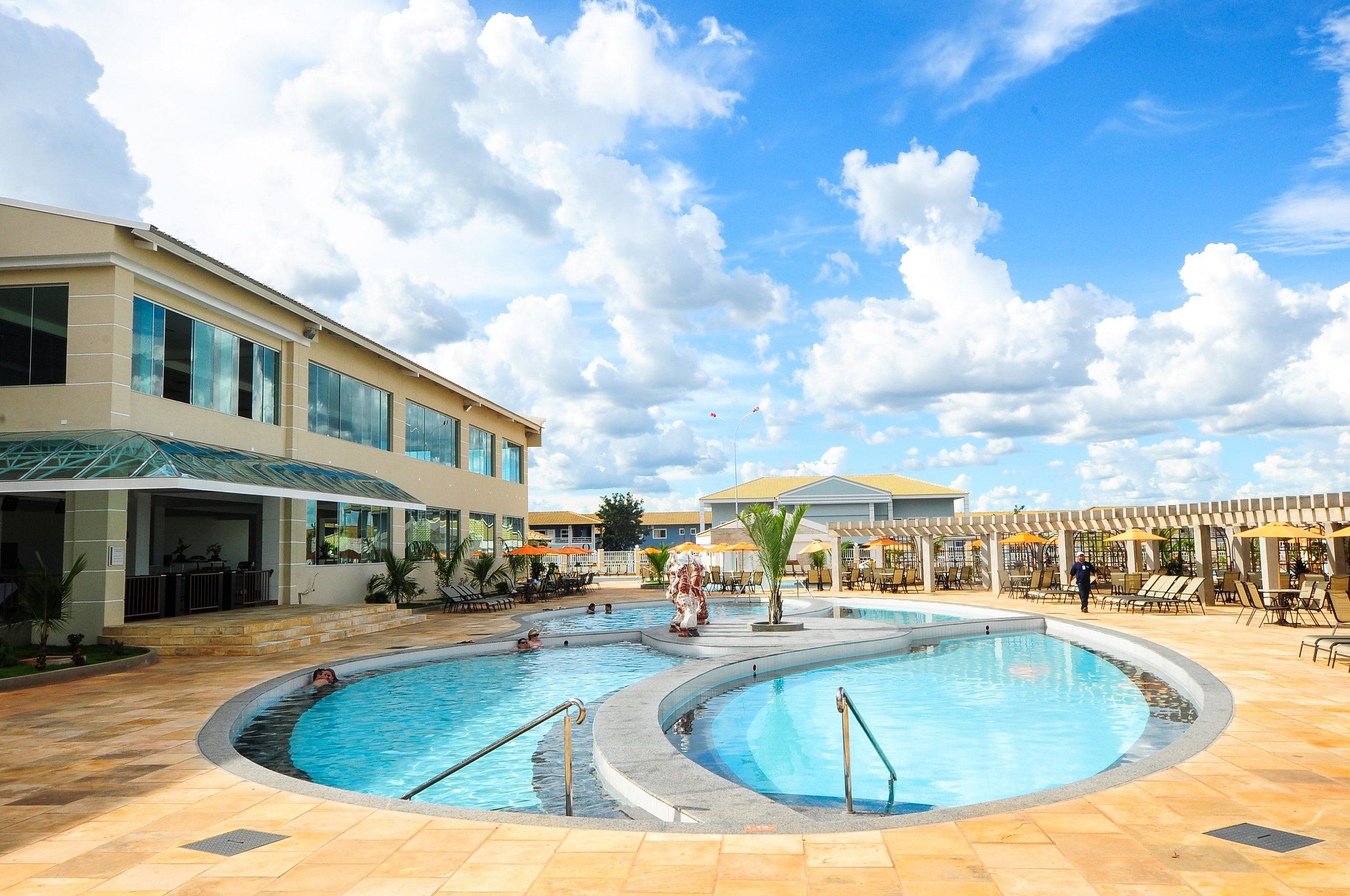 Uma área de piscina com várias piscinas, cadeiras de lounge e guarda-sóis.