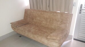 A beige sofa with a wooden armrest in a room with tiled flooring and a door with a handle. - LACQUA II (Caldas Novas)