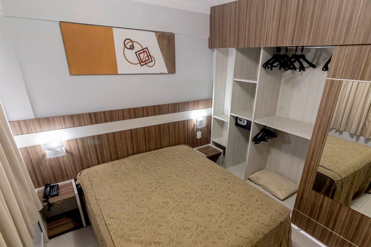 A hotel room with a bed, a wardrobe with hanging clothes, and a mirror.