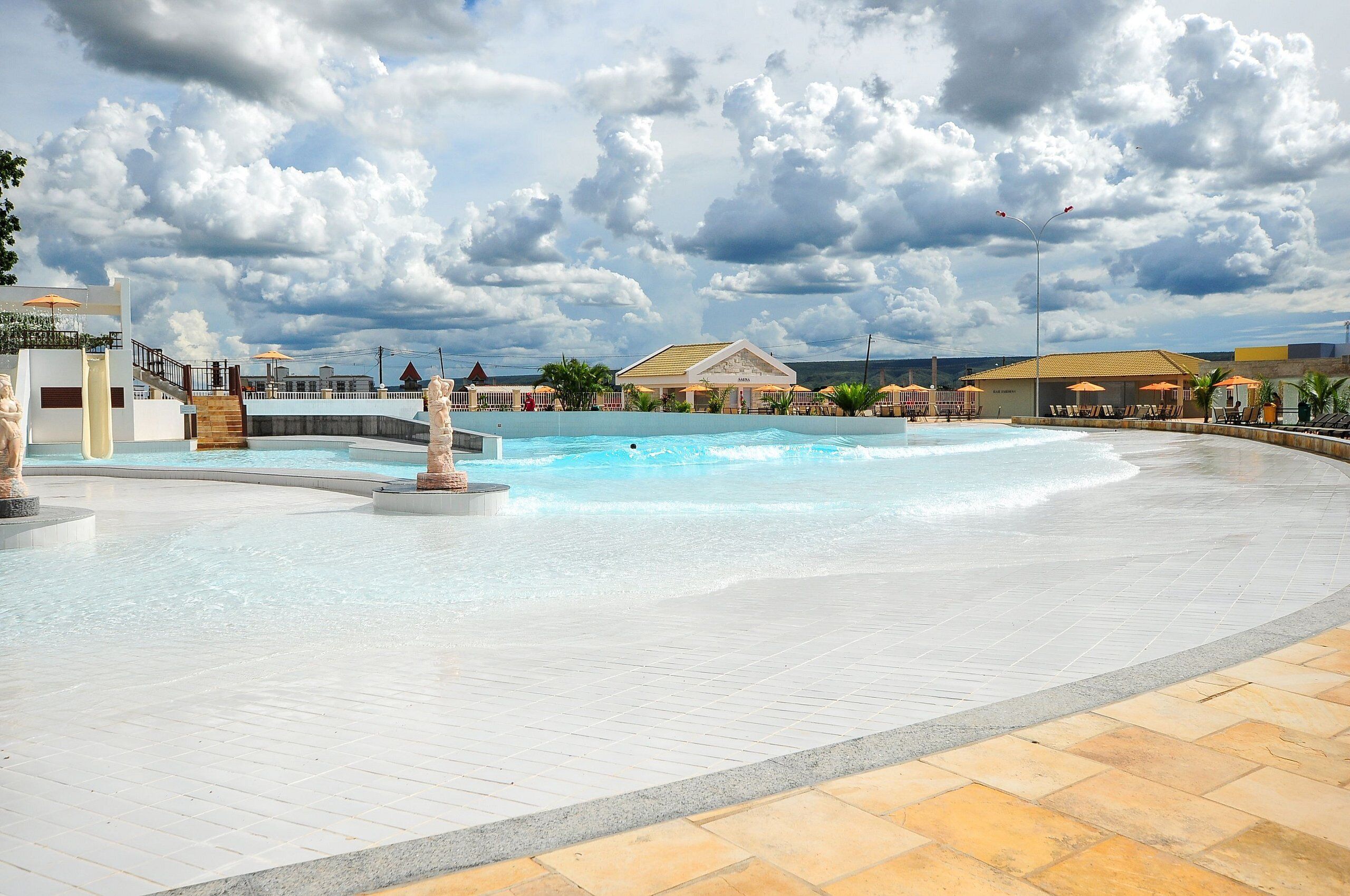 Ein Poolbereich mit einer Fontäne, Liegestühlen und einem Gebäude im Hintergrund.
