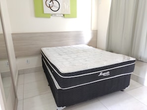 A neatly made bed with a white quilted mattress and a black base, positioned in a room with a light-colored tiled floor and a wooden headboard. - LACQUA II (Caldas Novas)