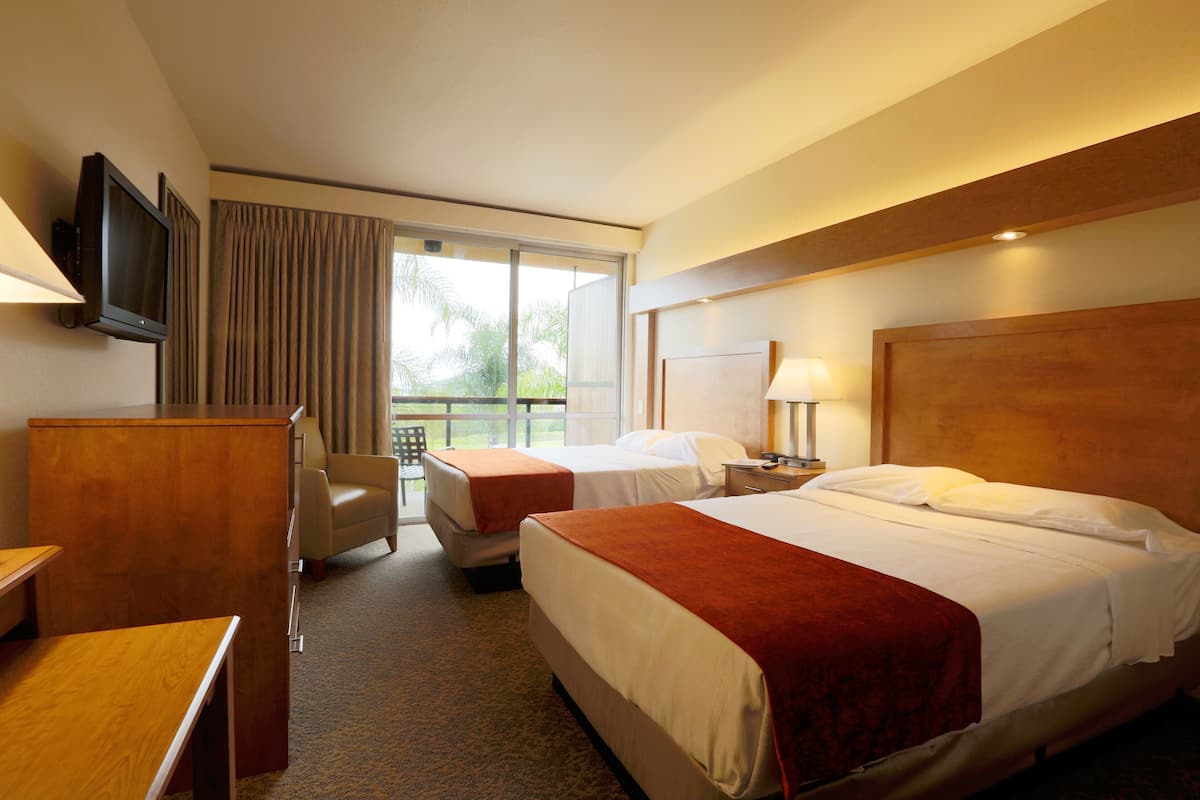 A hotel room with two beds, a desk, a chair, a television, and a window with curtains.