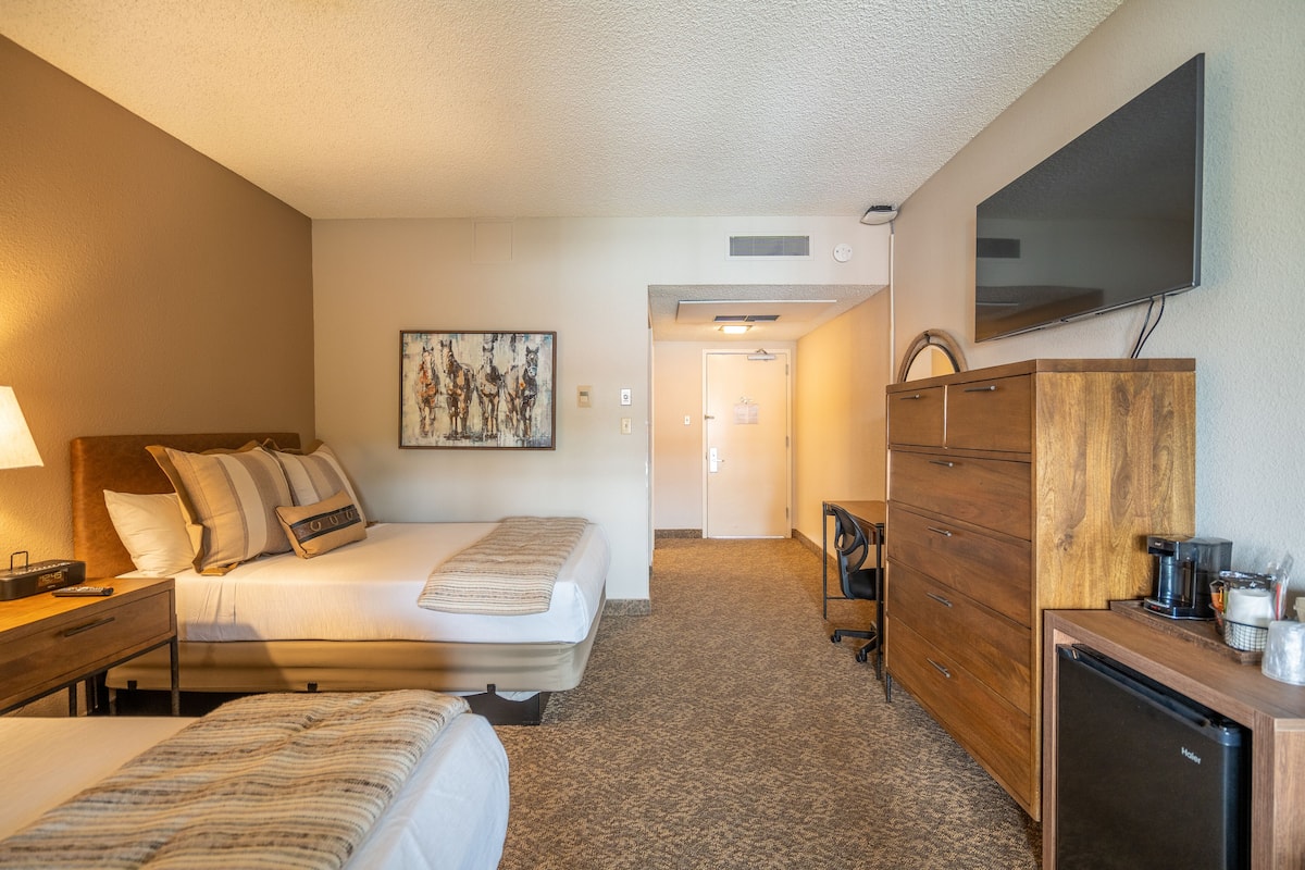 A hotel room with a bed, a desk, a dresser, a television, and a painting on the wall.