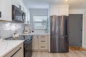 A modern kitchen with stainless steel appliances, white cabinetry, and a marble countertop.