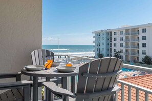 A balcony with a table, chairs, and a view of the ocean and a hotel building.