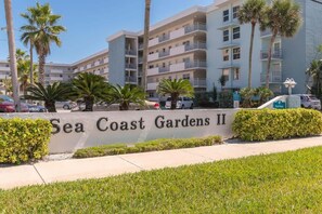 A multi-story building with balconies, palm trees, and a sign reading 'Sea Coast Gardens II.'