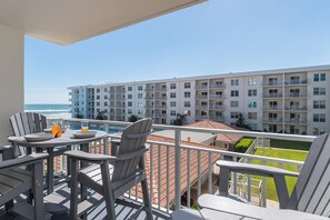A balcony with a pool table, chairs, and a view of a building with multiple balconies and a pool.