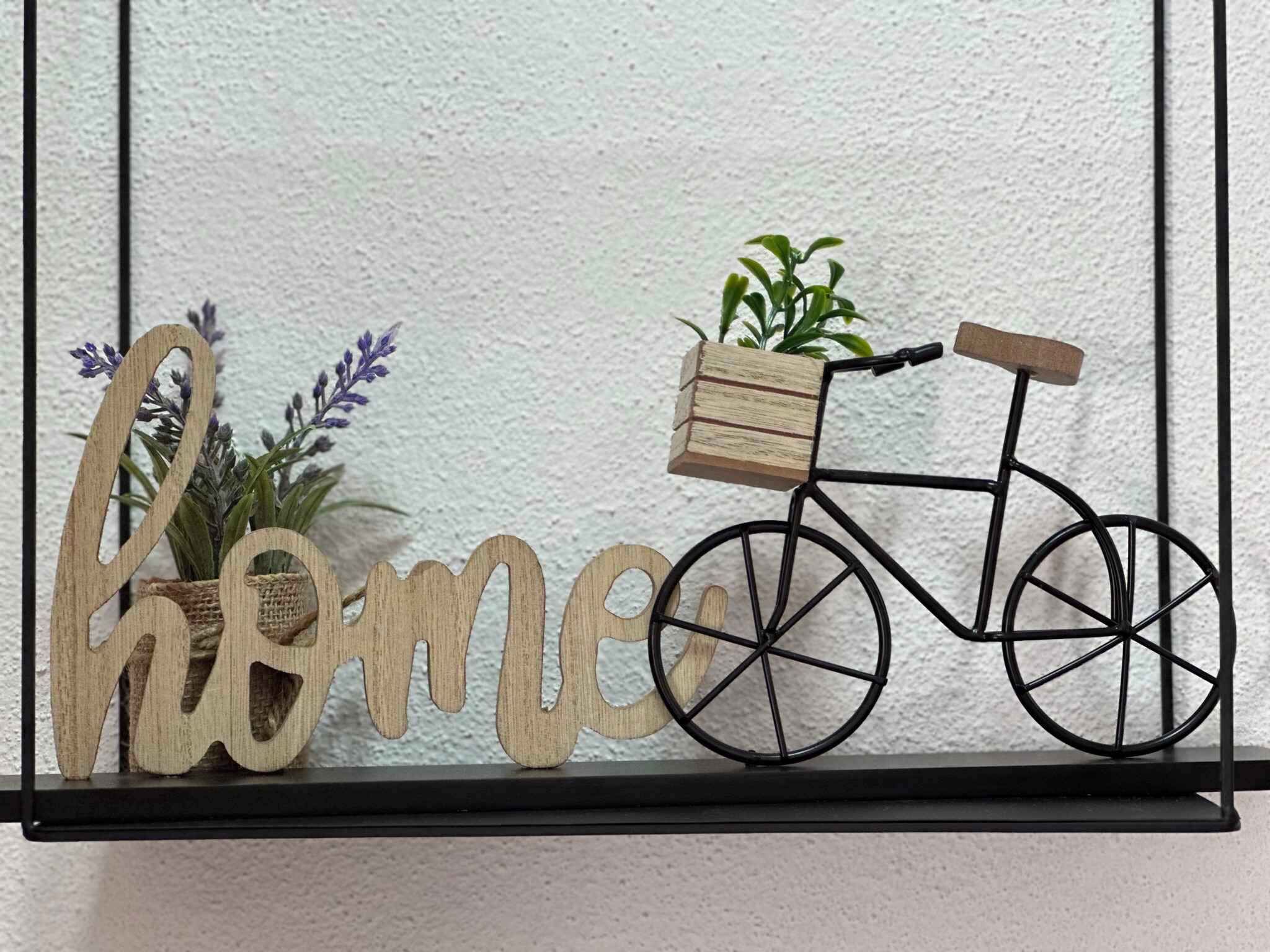 Un rètol de fusta amb la paraula 'home' i una bicicleta amb cistella, davant d'una paret amb relleu.
