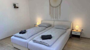 A double room with two beds, each with a pillow and a blanket, a bedside table with a lamp, and a wall hanging. - Villa with large pool- wheelchair accessible (Dobrinj)