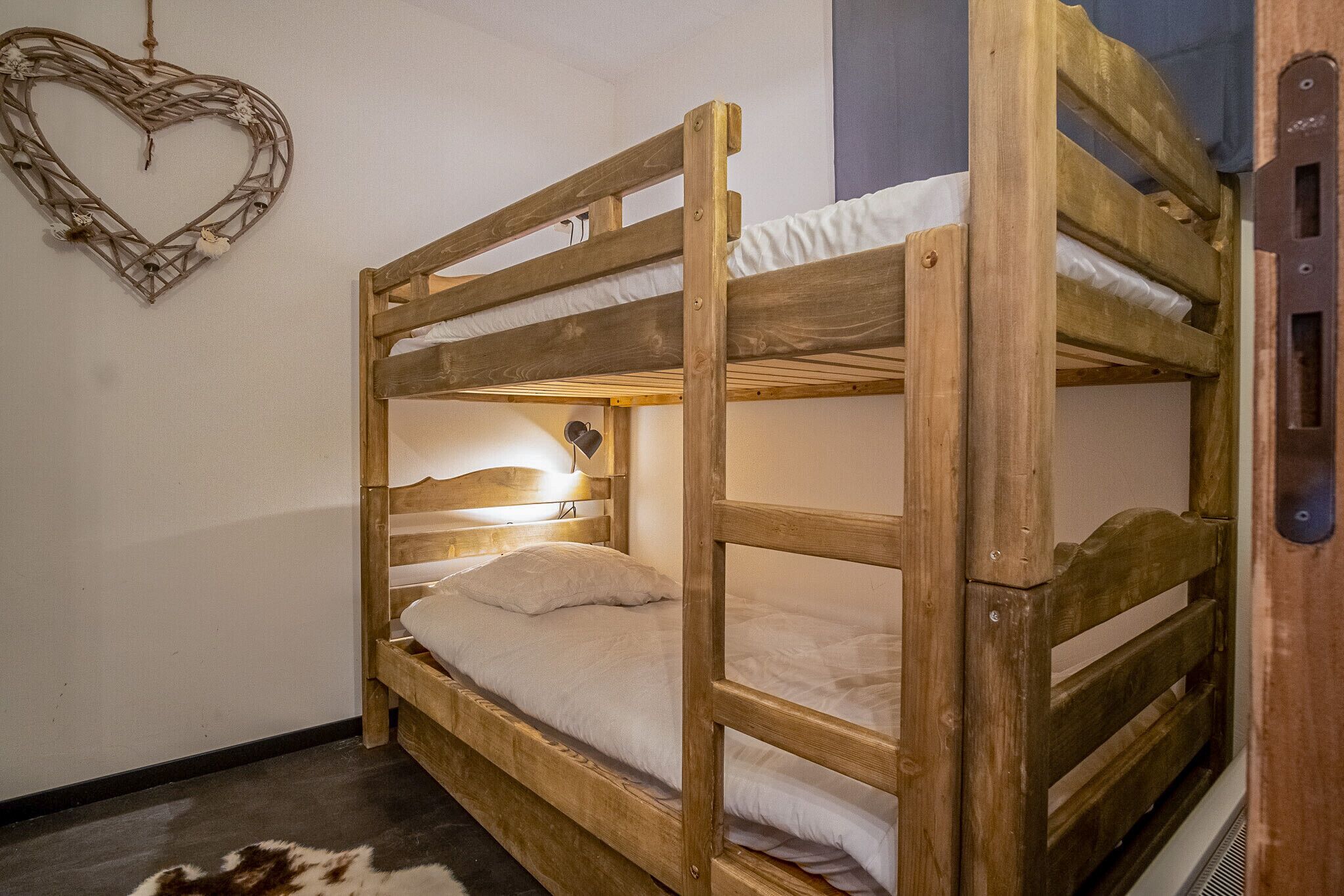 Un lit superposé avec une structure en bois, un matelas blanc et une tête de lit dotée d’un luminaire.
