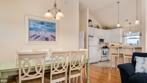 Un comedor con una mesa y sillas de vidrio, una cocina al fondo y un cuadro en la pared.