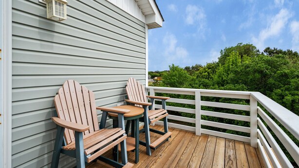Una terraza de madera con dos sillas Adirondack y una barandilla blanca.