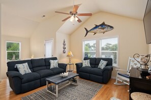 A living room with two dark sofas, a coffee table, a ceiling fan, and a fish wall art piece.