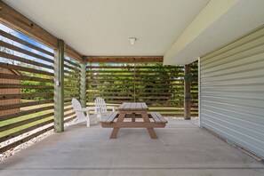 Ein überdachter Patio-Bereich mit Picknicktisch und Stühlen, umgeben von Holzleisten und einem Betonboden.