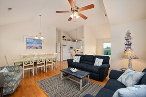 A spacious living room with a dark sofa, a coffee table, and a dining area with white chairs and a table. - Salada Sea Breeze: 5 min. walk to the beach, oceanside (Nags Head)
