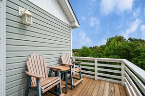 A wooden deck with two Adirondack chairs and a table, overlooking a green landscape. - Salada Sea Breeze: 5 min. walk to the beach, oceanside (Nags Head)