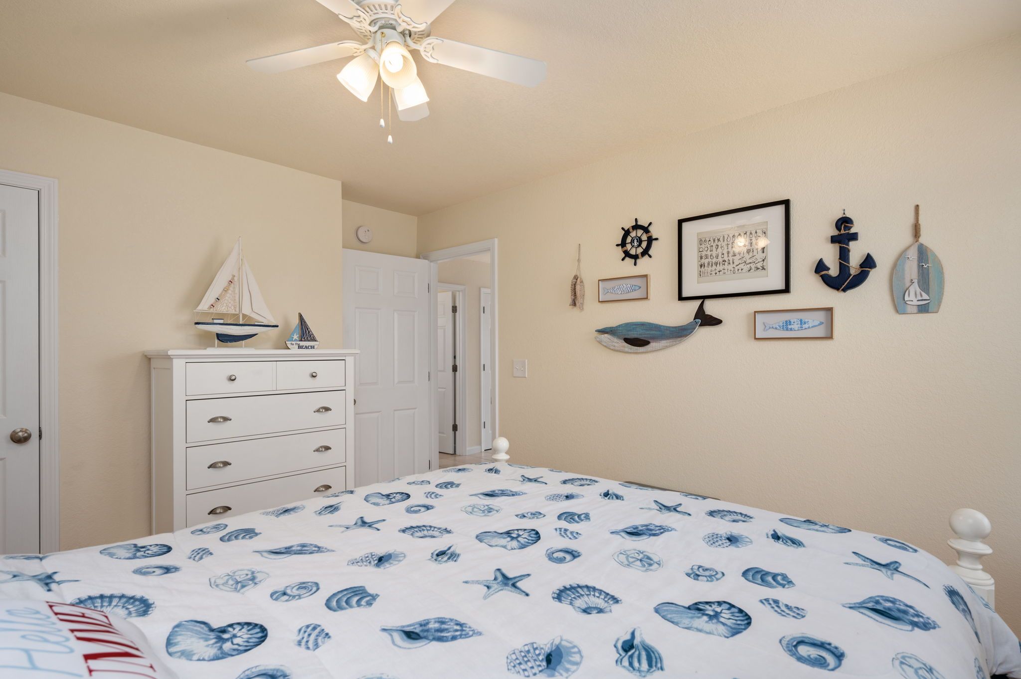 Une chambre à coucher comprenant un lit, une commode et des éléments de décoration murale, notamment des tableaux encadrés et un gouvernail de bateau.