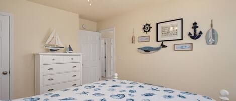Une chambre à coucher comprenant un lit, une commode et des éléments de décoration murale, notamment des tableaux encadrés et un gouvernail de bateau.