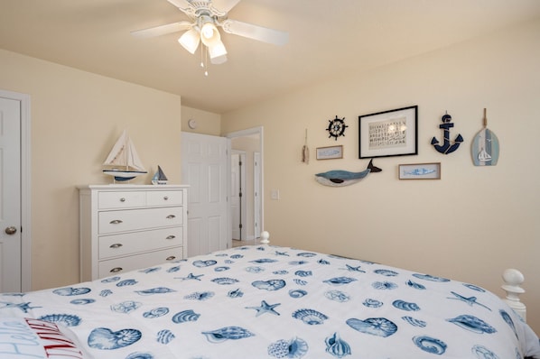 A bedroom with a bed, dresser, and wall decorations including framed pictures and a ship's wheel.