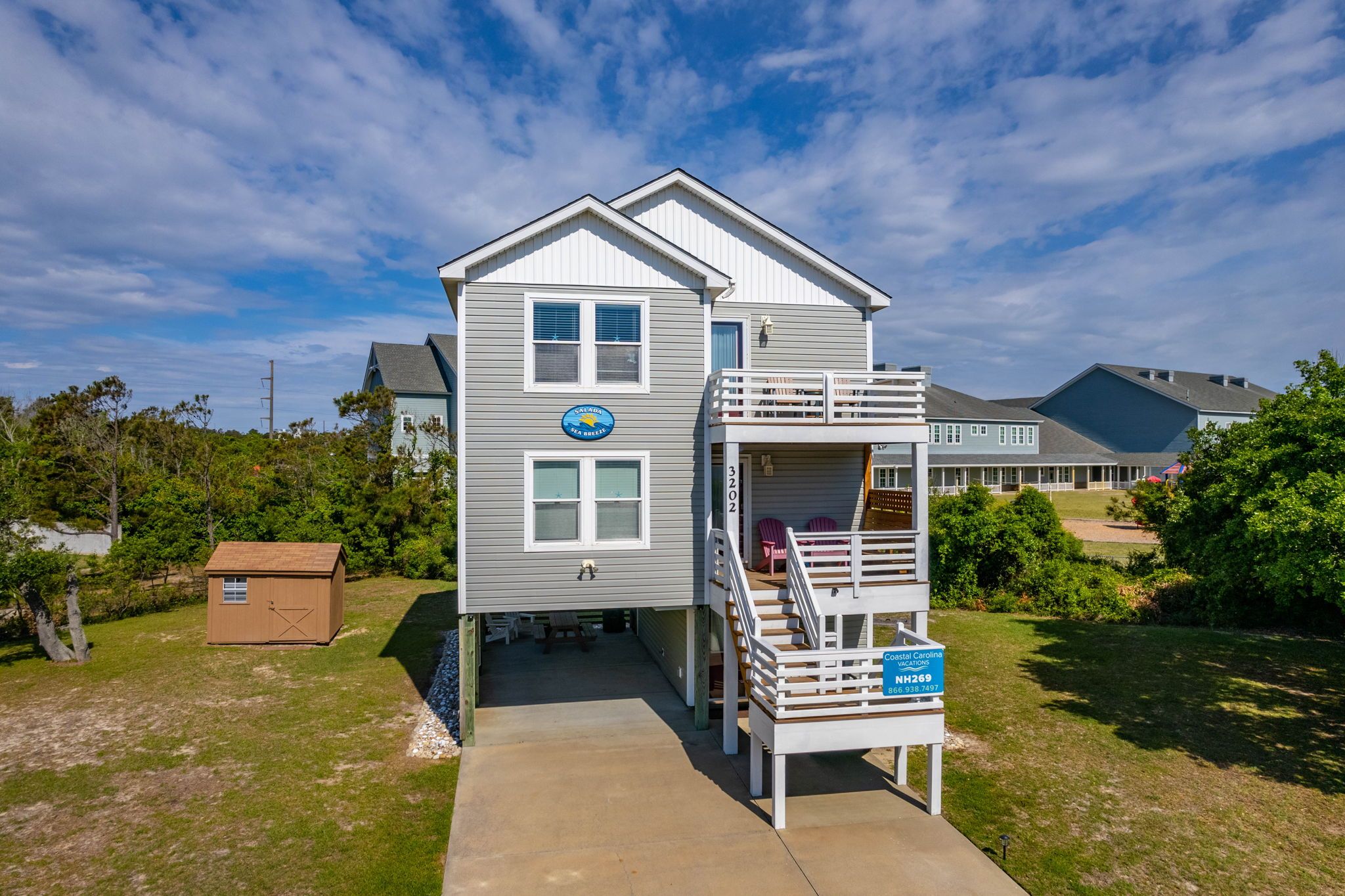 A two-story house with a balcony, a small deck, and a sign indicating Coastal Carolina Vacations.