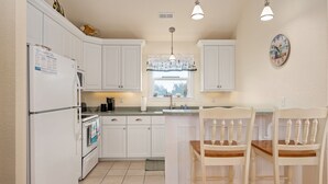 Una cocina con armarios blancos, un refrigerador, una estufa, un lavabo y dos sillas de madera.