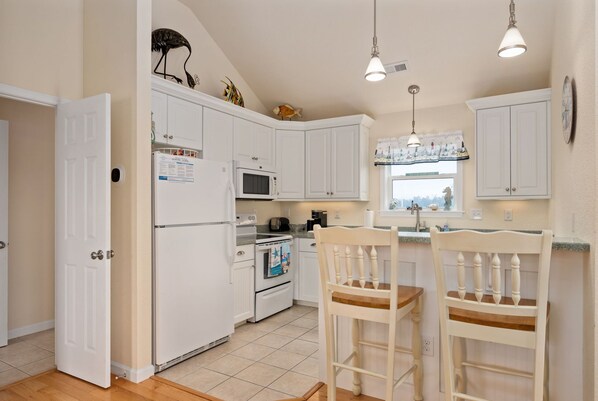A kitchen with white cabinets, a microwave, an oven, a refrigerator, two wooden chairs, and pendant lights. - Salada Sea Breeze: 5 min. walk to the beach, oceanside (Nags Head)