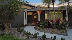 A residential house with a dark exterior, a front porch, and a landscaped garden with palm trees and various plants. - Palm Tree Paradise Tampa (Tampa)