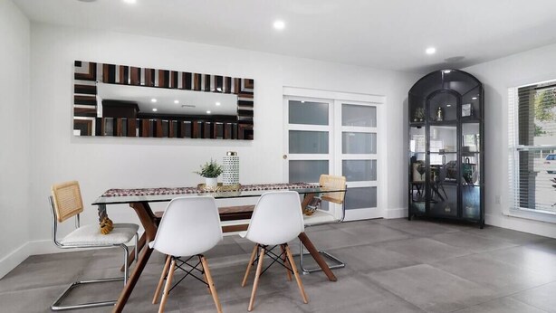A modern dining area with a glass table, white chairs, and a decorative wall unit. - Palm Tree Paradise Tampa (Tampa)